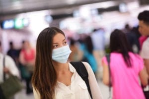 Person wearing protective mask against transmissible infectious diseases and as protection against pollution and the flu. Asian woman commuter in airport public area.